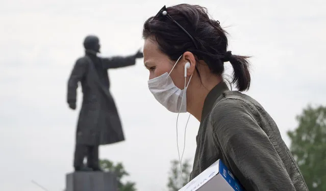 A woman wearing a face mask during a protect against coronavirus infection as she walks past a statue of Soviet Union founder Vladimir Lenin, in Kirovsk, about 30 kilometres (19 miles) east of St.Petersburg, Russia, Monday, June 8, 2020. (Photo by Dmitri Lovetsky/AP Photo)