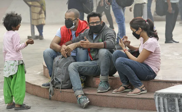 A girl begs for alms from a group of people wearing face masks to fight the pollution in New Delhi, India, Thursday, November 9, 2017. A thick gray haze has enveloped India's capital as air pollution hit hazardous levels, prompting local officials to shut down schools. According to a recent report by the Lancet medical journal on the impact of pollution across the world, one out of every four premature deaths in India in 2015, or some 2.5 million, was attributed to pollution. (Photo by Manish Swarup/AP Photo)