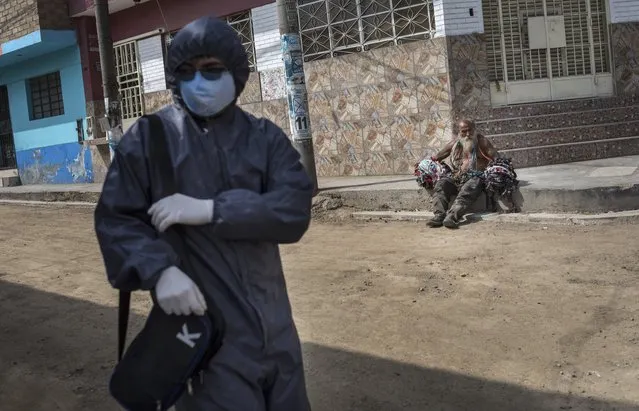 A commuter wearing a protective face mask as a measure to help curb the spread of the new coronavirus, waits for a bus while a homeless man sits on a curb on a street corner on the outskirts of Lima, Peru, Saturday, July 4, 2020. (Photo by Rodrigo Abd/AP Photo)