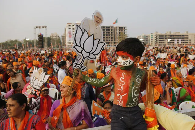 An Indian child with his body painted holds a cut out of Indian Prime Minister Narendra Modi with a symbol of the Bharatiya Janata Party (BJP) during an election campaign rally in Ahmadabad, India, Friday, December 8, 2017. Modi is on a two-day visit to Gujarat to campaign for the BJP in the Gujarat state assembly election which will be held on Dec. 9 and Dec. 14. Gujarati on the boy's body reads, “I am Gujarat – I am development”. (Photo by Ajit Solanki/AP Photo)