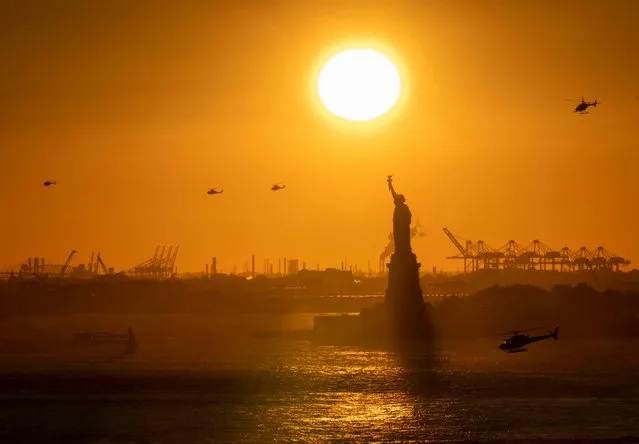 Helicopters fly in the distance as the sun sets behind the Statue of Liberty in New York on November 3, 2022. (Photo by Angela Weiss/AFP Photo)