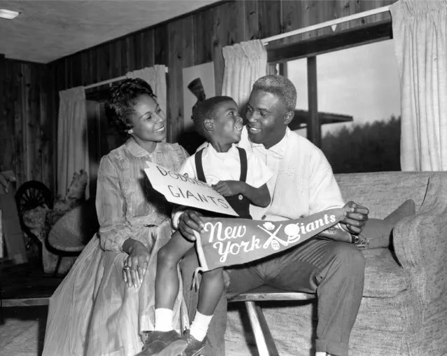 Jackie Robinson, Brooklyn Dodgers star since breaking into Major League baseball in 1947, is shown with his wife, Rachel, and their four-year-old son, Jackie Jr., in their home in Stamford, Conn., December 13, 1956.  Robinson, 37, holds a banner for the rival New York Giants baseball club to which he was traded for relief pitcher Dick Littlefield and $35,000 in cash.  Robinson retired in January, voiding the trade. (Photo by John Lindsay/AP Photo)