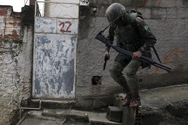 In this Friday, February 23, 2018 photo, a soldier jumps from an uneven walkway under the clamor of a barking dog during a surprise operation at the Vila Kennedy slum in Rio de Janeiro, Brazil. On the rise for at least two years, violence in Rio appeared to reach a tipping point during Carnival celebrations earlier this month. The governor pleaded for federal help, and President Michel Temer issued a presidential decree that put the military in charge of Rio's police. (Photo by Leo Correa/AP Photo)