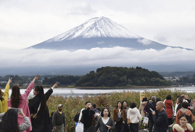 People look at Mount Fuji, covered with its first snow of the season in Fujikawaguchiko, Japan on October 23, 2025. (Photo by Kyodo News/Reuters)