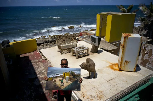 Roberto Figueroa Caballero holds a printed photo taken on October 5, 2017 of him amid his seaside home that was destroyed by Hurricane Maria, as he stands on the same property with his pet dog in the La Perla neighborhood of San Juan, Puerto Rico, May 29, 2018. Figueroa, who found a job at a pizzeria, aims to rebuild his home and is appealing FEMA's second rejection of his application. Figueroa's dog was not allowed to go with him to a donated apartment where he lives now, so he visits his property daily to feed and care for him. (Photo by Ramon Espinosa/AP Photo)