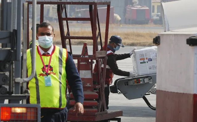A Nepalese airport ground staff unload a box carrying AstraZeneca/Oxford University vaccine, manufactured under license by Serum Institute of India, arrive at Tribhuwan International Airport in Kathmandu, Nepal, Thursday, January 21, 2021. India sent 1 million doses of a coronavirus vaccine to Nepal on Thursday, a gift that is likely to help repair strained ties between the two neighbors. (Photo by Niranjan Shrestha/AP Photo)