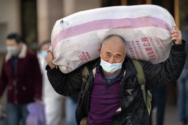 A traveler wearing a face mask to protect against the spread of the coronavirus carries his luggage as he walks out of an exit at the Beijing Railway Station in Beijing, Thursday, January 28, 2021. (Photo by Mark Schiefelbein/AP Photo)