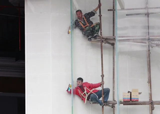 Workers install the glass wall of a building under construction in Guangzhou, Guangdong province, February 5, 2015. (Photo by Alex Lee/Reuters)