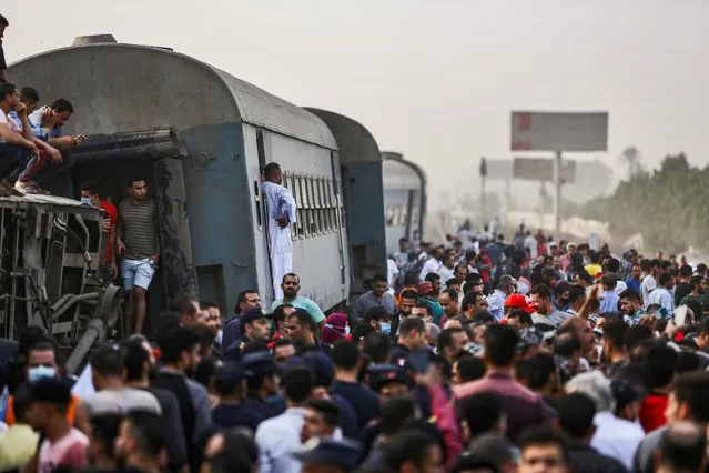 People gather by an overturned train carriage at the scene of a railway accident in the city of Toukh in Egypt's central Nile Delta province of Qalyubiya on April 18, 2021. The train accident in Egypt left 97 wounded on April 18 after it derailed off its tracks heading northwards from the capital Cairo, the health ministry said, in the latest railway disaster. Eight carriages derailed off the tracks as the train headed to Mansoura, about 130 kilometres north of Cairo. (Photo by Ayman Aref/AFP Photo)