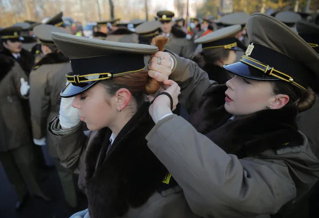 A military cadet gets help from a colleague to adjust her hair before taking part the military parade in Bucharest, Romania, Saturday, December 1, 2018. (Photo by Vadim Ghirda/AP Photo)