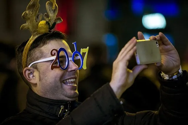 A man makes a photo with his smartphone as he attends for the New Year's Eve celebrations at the Puerta del Sol square in Madrid, Spain, on 31 December 2016. This year the police have placed obstacles, such as planters, bollards and heavy vehicles, to prevent attacks. In total, more than 800 personnel are involved in the security system, of which 400 are national police officers and 400 municipal police. (Photo by Santi Donaire/EPA)