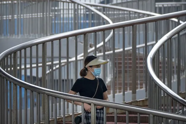 A woman wearing a face mask to protect against COVID-19 walk across a pedestrian bridge during the morning rush hour in Beijing, Wednesday, August 4, 2021. (Photo by Mark Schiefelbein/AP Photo)