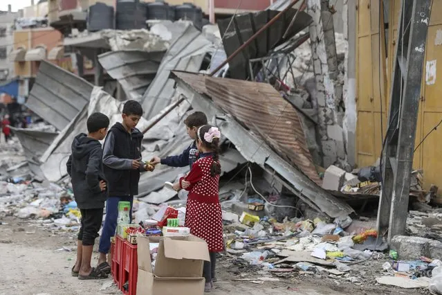 Palestinian children sell sweets in front of the rubble of a destroyed building in Jebaliya refugee camp, Gaza Strip, Tuesday, November 28, 2023, on the fifth day of the temporary ceasefire between Hamas and Israel. (Photo by Mohammed Hajjar/AP Photo)