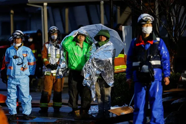 People covered in emergency blankets watch a rescue operation in Wajima, Ishikawa prefecture, Japan on January 3, 2024. (Photo by Kim Kyung-Hoon/Reuters)