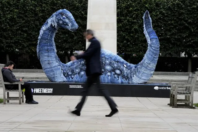 A man walks past “Messy” the COP Ness Monster in a park in London, Thursday, October 28, 2021. The five-metre-long sculpture has been created completely sustainably, with “bones” made from steel, plywood and wire mesh, and “skin” made from recycled jeans to raise awareness of the polluting effects of denim on the environment. (Photo by Frank Augstein/AP Photo)