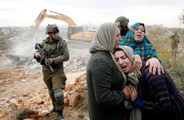 A Palestinian woman is comforted as she reacts while an Israeli machinery demolishes her under-construction house, in Hebron, in the Israeli-occupied West Bank, December 28, 2021. (Photo by Mussa Qawasma/Reuters)