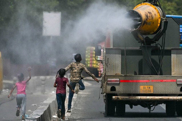 Children run behind a truck spraying water along a street on a hot summer day in New Delhi on May 28, 2024. (Photo by Arun Sankar/AFP Photo)