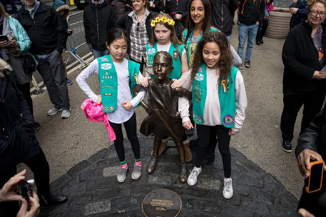 Young members of Girl Scout troop 3484 pose for photos with the “Fearless Girl” statue, March 27, 2017 in New York City. New York City Mayor Bill De Blasio announced that the popular statue of a young girl staring down the famous Wall Street “Charing Bull” will stay in place until February 2018. (Photo by Drew Angerer/Getty Images)
