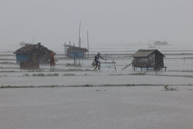 People walk along shrimp and crab farms that are flooded due to heavy rain as Cyclone Remal passes the country, in the Shyamnagar area of Satkhira, Bangladesh on May 27, 2024. (Photo by Mohammad Ponir Hossain/Reuters)