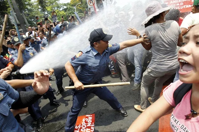 An anti-riot policeman reaches to grab a protester as they are hit with a water cannon during a protest against the upcoming visit of U.S. President Barack Obama next week, in front of the U.S. embassy in Manila April 23, 2014. (Photo by Romeo Ranoco/Reuters)