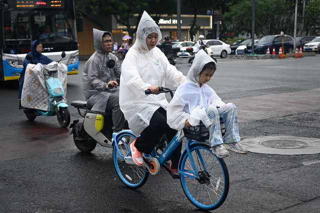 A raincoat-clad child rides in the front basket of a bicycle on a rainy day in Beijing on July 2, 2024. (Photo by WANG Zhao/AFP Photo)