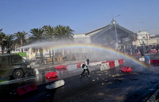 In this Monday, May 1, 2017 photo, a rainbow is formed in the mist of a police water cannon as a masked, female protester runs during clashes at a May Day demonstration in Santiago, Chile. (Photo by Esteban Felix/AP Photo)