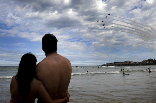 Beach-goers watch as C-101 Aviojets from the Spanish Air Force aerobatic group Patrulla Aguila fly over San Lorenzo beach during an aerial exhibition in Gijon, northern Spain, July 26, 2015. (Photo by Eloy Alonso/Reuters)