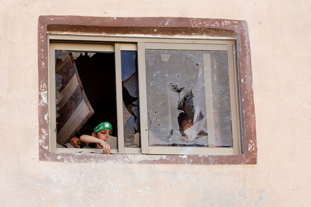 A Palestinian boy wearing the headband of Qassam brigades, the armed wing of Hamas, looks out of a damaged window with another child during an Israeli raid, in Tubas, in the Israeli-occupied West Bank, on August 14, 2024. (Photo by Raneen Sawafta/Reuters)