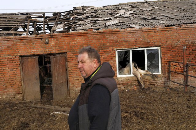 Farmer Oleksandr Novikov, 58, stands next to a dead cow in the window of a damaged barn in Vilhivka village, amid Russia's attack on Ukraine, near Kharkiv, Ukraine, May 11, 2022. (Photo by Ricardo Moraes/Reuters)