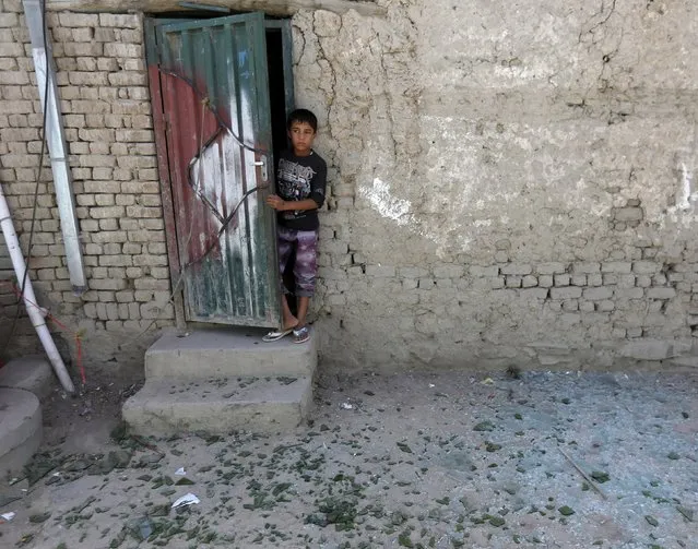 A boy stands at the door of his house in front of broken glasses scattered on the ground near the site of a car bomb blast at the entrance gate to Kabul airport, Afghanistan August 10, 2015. (Photo by Mohammad Ismail/Reuters)