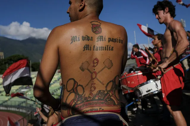 In this November 28, 2019 photo, a member of the Caracas FC fan club's tattoo reads in Spanish “Mi life. My passion. My family” above the team's coat of arms, as he plays a drum in the stands before a game at Estadio Olimpico in Caracas, Venezuela. The Caracas Football Club became champion of the Venezuela League this year. (Photo by Matias Delacroix/AP Photo)
