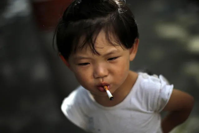 A girl stands on a sidewalk after putting an unlit cigarette in her mouth, which she picked up from the ground, in Shanghai July 31, 2014. (Photo by Carlos Barria/Reuters)