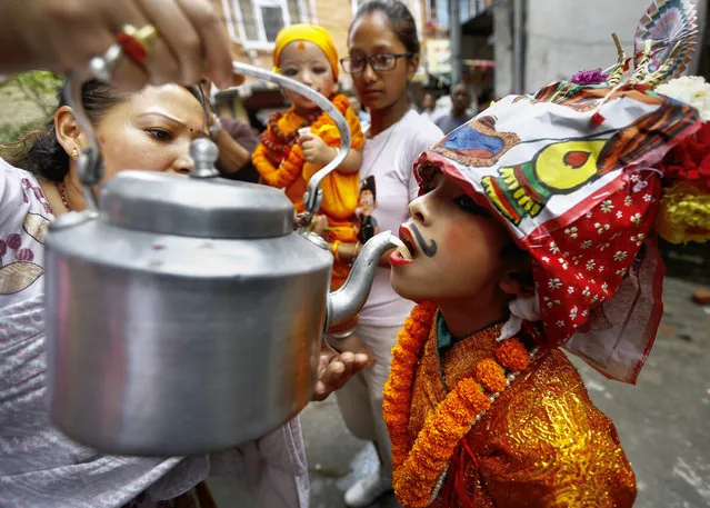 A Nepalese boy wearing festive attire drinks cow milk before attending a procession of the Gai Jatra (Cow Festival) in Kathmandu, Nepal, August 11, 2014. The Gai Jatra is dedicated to family members who have passed away recent years. (Photo by Narendra Shrestha/EPA)