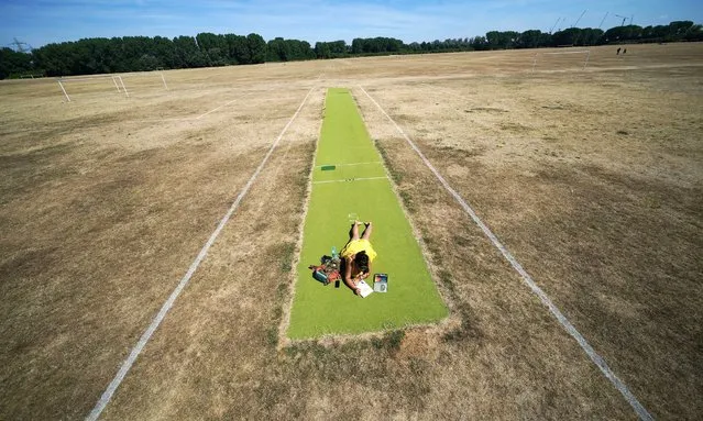 A woman relaxes on a green cricket pitch surrounded by parched football pitches, on Hackney Marshes, east London on Saturday, August 6, 2022. (Photo by Yui Mok/PA Images via Getty Images)