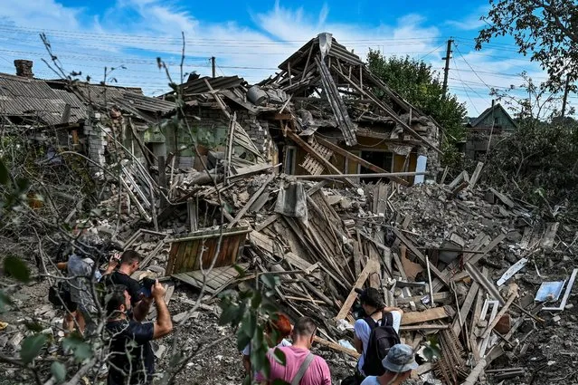 People stand next to a residential house destroyed by a Russian missile strike in the settlement of Kushuhum, as Russia's attack on Ukraine continues, in Zaporizhzhia region, Ukraine on August 10, 2022. (Photo by Dmytro Smolienko/Reuters)
