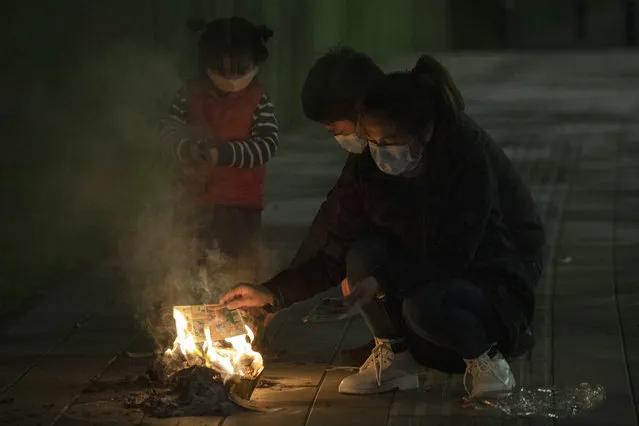 A family burn paper offerings for their departed relatives on the streets of Wuhan in central China's Hubei province on Saturday, April 4, 2020. Authorities are controlling access and limiting the number of people entering cemeteries across China during the annual Qingming festival, also known as the Grave Sweeping Day, a day when Chinese around the world remember their dearly departed and take time off to clean up the tombs and place flowers and offerings, a move to prevent the spread of the new coronavirus outbreak. (Photo by Ng Han Guan/AP Photo)