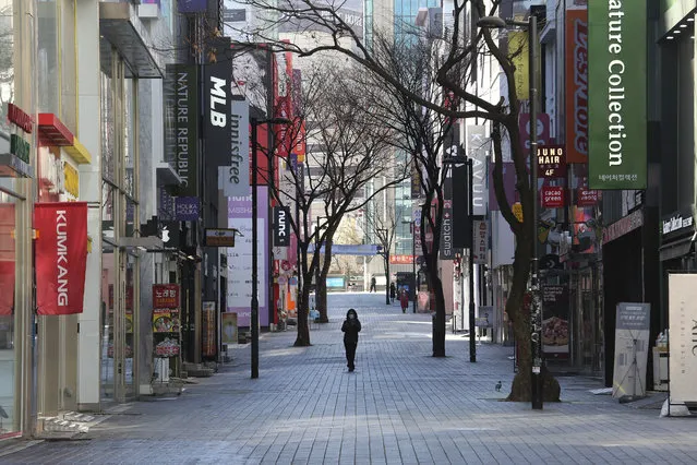 A woman wearing a face mask against the coronavirus walks along on a nearly empty shopping street in Seoul, South Korea, Sunday, March 22, 2020. (Photo by Ahn Young-joon/AP Photo)