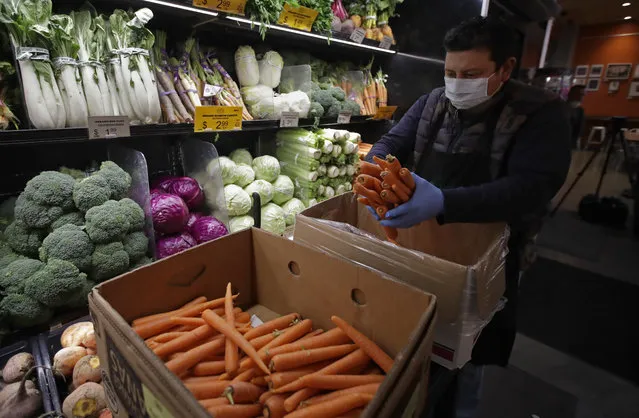 A worker, wearing a protective mask and gloves against the COVID-19 coronavirus, stocks produce before the opening of Gus's Community Market, Friday, March 27, 2020, in San Francisco. Health experts say there's no evidence the new coronavirus is spread through food. That's because organisms take different biological paths to sicken people. (Photo by Ben Margot/AP Photo)