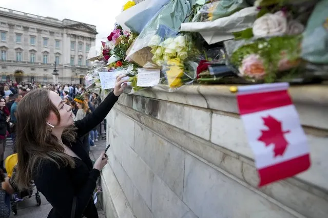 A woman places flowers and a note as long lines of mourners form to pay their respect at the gates of Buckingham Palace in London on Friday, September 9, 2022. Queen Elizabeth II, Britain's longest-reigning monarch and a rock of stability across much of a turbulent century, died Thursday Sept. 8, 2022, after 70 years on the throne. She was 96. (Photo by Nathan Denette/The Canadian Press via AP Photo)