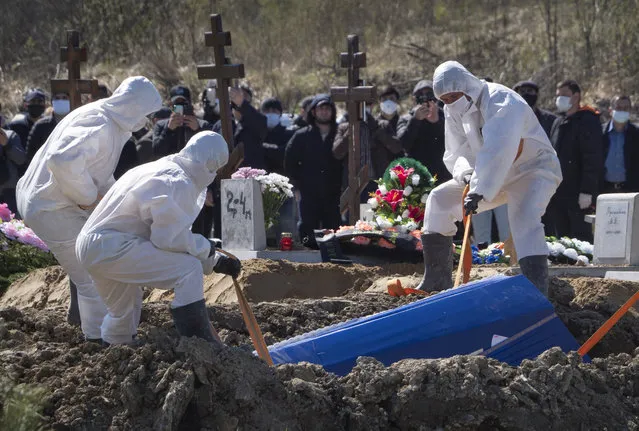 Grave diggers wearing protective suits bury a COVID-19 victim as relatives and friends stand at a safe distance, in the special purpose for coronavirus victims section of a cemetery in Kolpino, outside St.Petersburg, Russia, Sunday, May 10, 2020. (Photo by Dmitri Lovetsky/AP Photo)