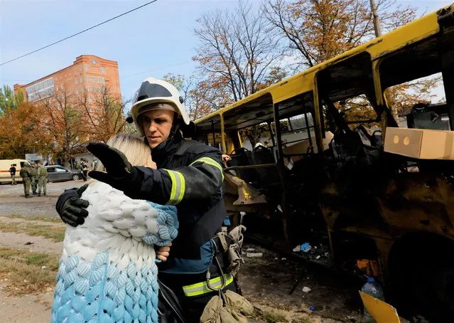 A firefighter comforts a woman next to the destroyed bus in which her teenage child was killed by shelling near a local market during Russia-Ukraine conflict in Donetsk, Ukraine on September 22, 2022. (Photo by Alexander Ermochenko/Reuters)