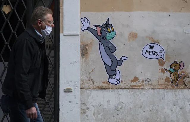 A man wearing a face mask walks past a mural by street artist Maupal, created to pay homage to late Gene Deitch, the author of “Tom and Jerry” in Rome on April 29, 2020, during the country's lockdown aimed at curbing the spread of the COVID-19 infection, caused by the novel coronavirus. (Photo by Tiziana Fabi/AFP Photo)