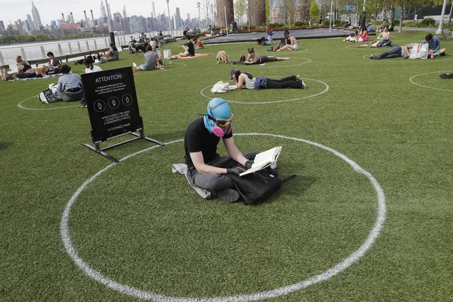 Ridley Goodside wears a rubber diving head covering along with goggles and a special air filtration mask to protect himself from the spread of coronavirus as he sits in a designated circle marked on the grass at Brooklyn's Domino Park during the current coronavirus outbreak, Monday, May 18, 2020, in New York. The circles were added after the park became severely overcrowded during a spate of unseasonably warm weather just over a week ago. Goodside said he's been protecting himself since he first heard about the virus much earlier this year. (Photo by Kathy Willens/AP Photo)