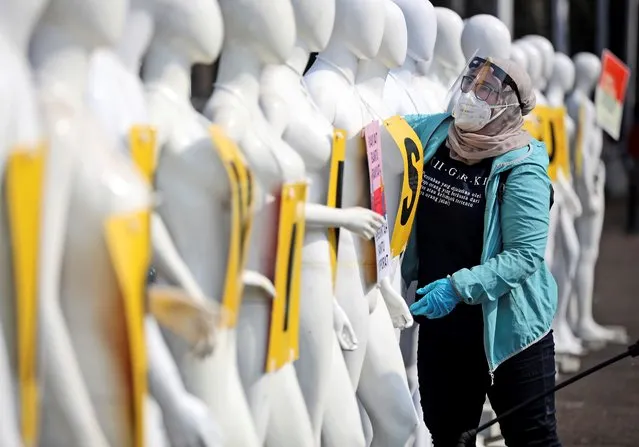 A Greenpeace activists wearing protective gear to help curb the spread of the coronavirus arranges mannequins used to display posters during a protest outside the parliament in Jakarta, Indonesia, Monday, June 29, 2020. About a dozen of activists staged the protest against the government's omnibus bill on job creation that was intended to boost economic growth and create jobs, saying that it undermined labor rights and environmental protection. (Photo by Dita Alangkara/AP Photo)