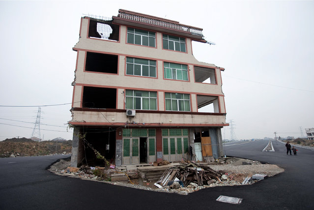 A woman and child walk past a house sit in the middle of a newly built road in Wenling city in east China's Zhejiang province Thursday, November 22, 2012. The house belongs to an elderly man, who refused to sign an agreement to allow his house to be demolished by the authorities, as the compensation offered to him is not enough, according to local media. (Photo by AP Photo)