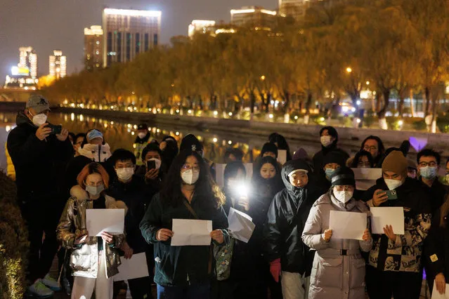 People gather for a vigil and hold white sheets of paper in protest over coronavirus disease (COVID-19) restrictions, during a commemoration of the victims of a fire in Urumqi, as outbreaks of COVID-19 continue, in Beijing, China on November 27, 2022. (Photo by Thomas Peter/Reuters)