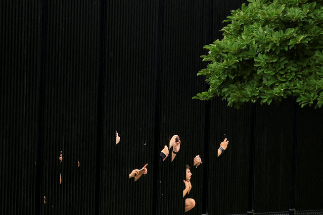 Tourists reach through fencing with their phones to photograph the White House after President Trump cut his G7 trip short and returned to Washington on June 17, 2025. (Photo by Kevin Mohatt/Reuters)