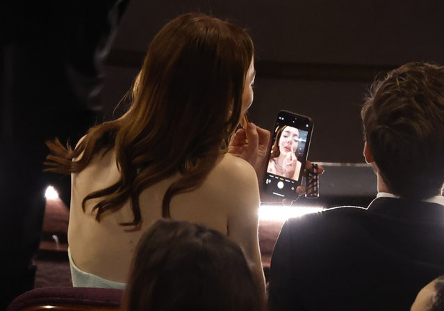 American actress Emma Stone uses her mobile phone to touch up her makeup during the 96th annual Academy Awards ceremony at the Dolby Theatre in the Hollywood neighborhood of Los Angeles, California, USA, 10 March 2024. The Oscars are presented for outstanding individual or collective efforts in filmmaking in 23 categories. (Photo by Caroline Brehman/EPA/EFE)