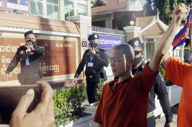 Theary Seng, center, a Cambodian-American lawyer, dressed in a prison-style orange outfit, raises her arm with her supporter as she arrived at Phnom Penh Municipal Court in Phnom Penh, Cambodia, Tuesday, January 4, 2022. Cambodian security forces on Tuesday briefly detained Theary Seng, a prominent rights activist, as she walked barefoot near the prime minister‚ residence in Phnom Penh, wearing the orange outfit and Khmer Rouge-era ankle shackles. She was released, shortly afterwards, and arrived at the Phnom Penh court for the resumption of her trial on treason charges. (Photo by Heng Sinith/AP Photo)