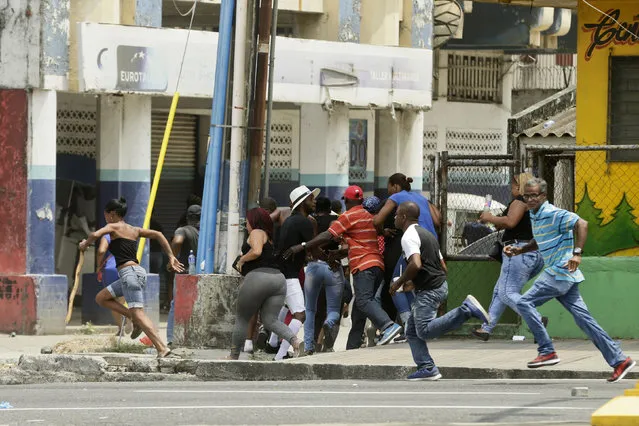 People run for cover as Panamanian police shoot rubber bullet into the air to disperse protesters from splinter groups who were throwing rocks at police and erecting burning barricades, in Colon, Panama, Tuesday, March 13, 2018. A march was called by a social and union movement to protest what they see as the slow pace of a multimillion-dollar plan to revitalize Colon’s collapsed sewer system, water supply and housing. (Photo by Arnulfo Franco/AP Photo)